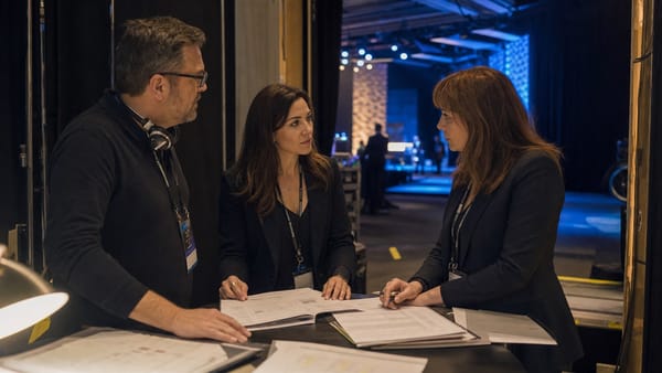 Equipo de operaciones conversa junto a materiales de producción después de una conferencia, con el escenario vacío al fondo.