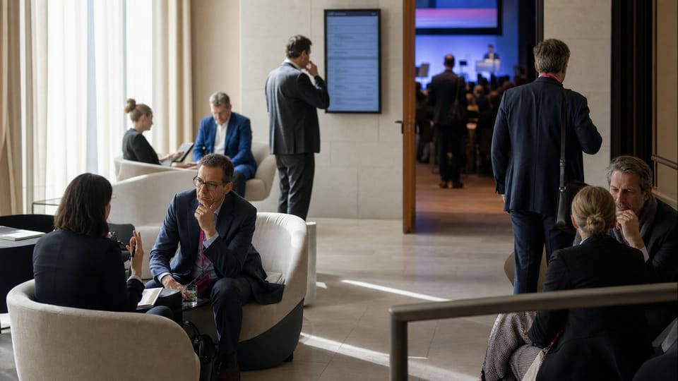 Asistentes conversan y reflexionan en una zona tranquila junto a un auditorio durante una pausa de conferencia.